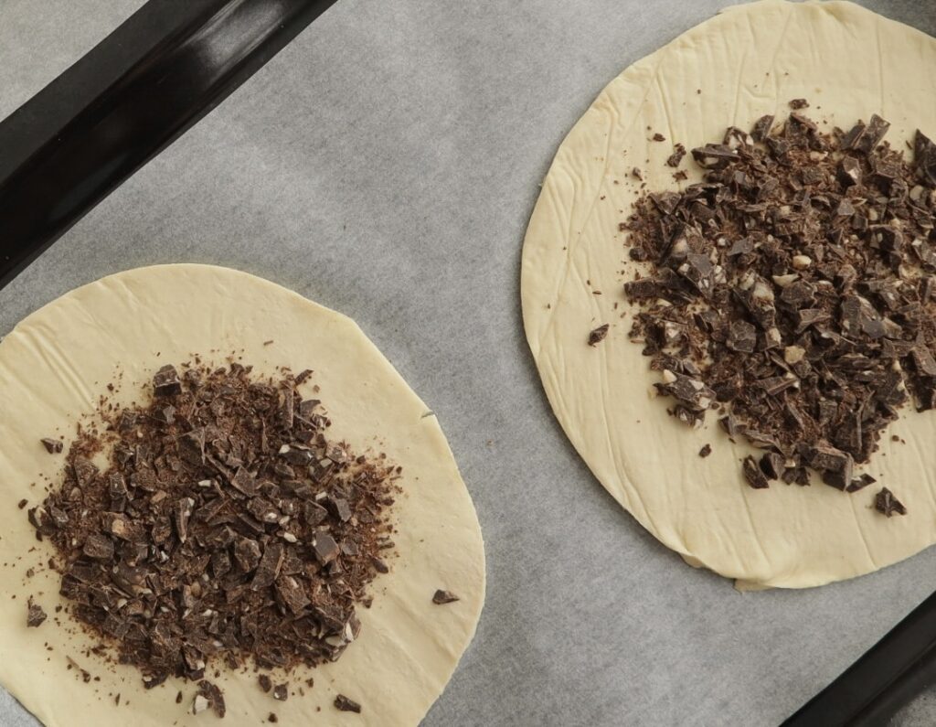 Two rounds of puff pastry topped with chocolate on parchment paper