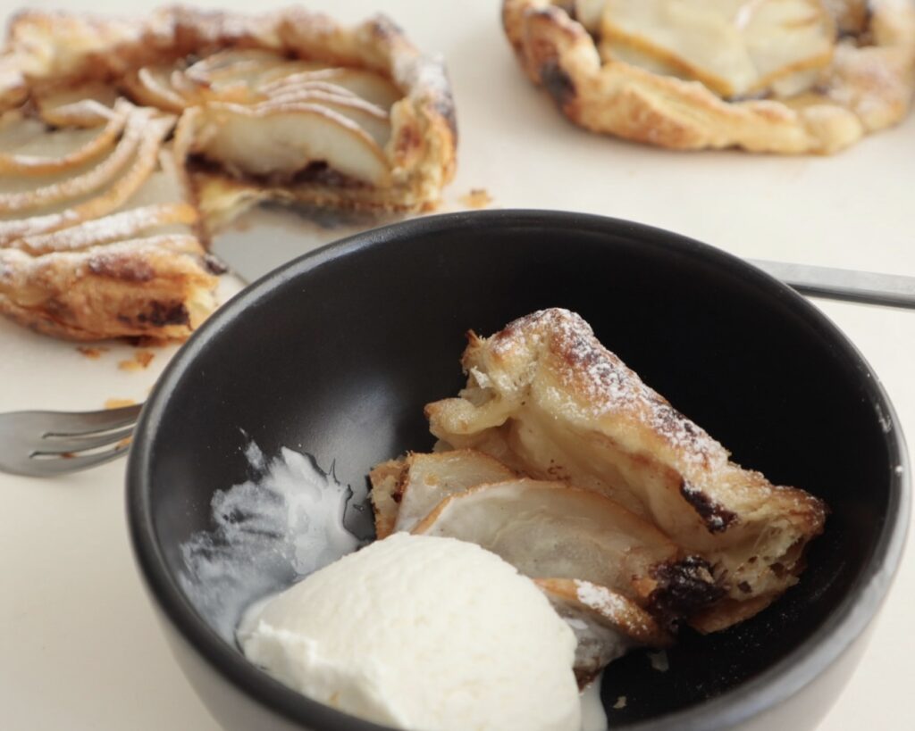 A slice of pear galette in a bowl, served with vanilla ice cream