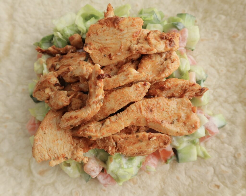 Cooked chicken and salad placed on a tortilla wrap