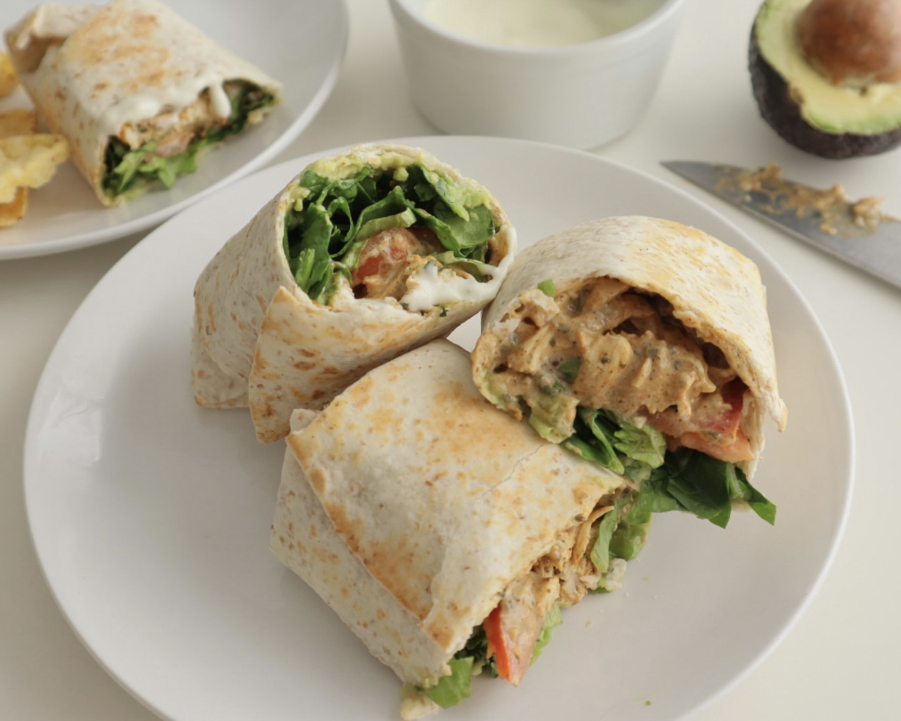 Chicken korma wrap with avocado and extra sauce in the background